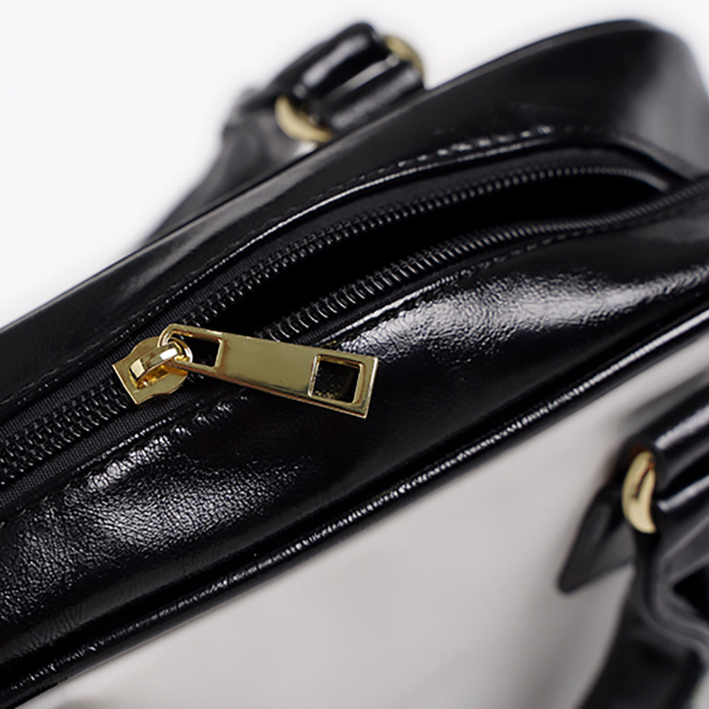 Close-up of a black handbag with gold zipper and hardware on a white background